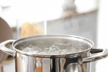 Mutfaktaki ocağın üstünde kaynar su bulunan paslanmaz çelik tencere, yakın plan.