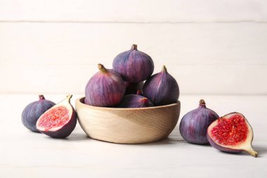 Beyaz ahşap arka planda taze olgun incirlerle dolu bir kâse.