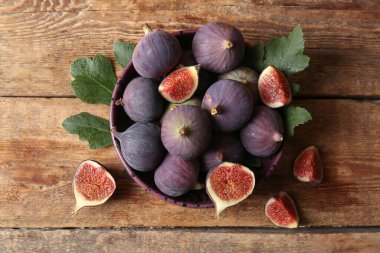 Tahta arka planda taze incir ve yapraklarla dolu bir kâse.