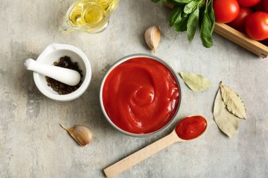 Bir kase lezzetli domates sosu ve gri arka planda farklı malzemeler.