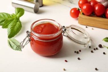 Fesleğen yapraklı bir kavanoz lezzetli domates sosu ve beyaz arka planda biber, yakın plan.