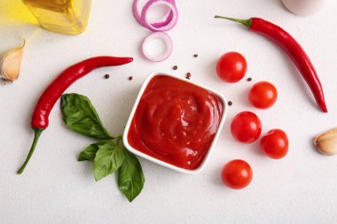 Bir kase lezzetli domates sosu ve beyaz arka planda farklı malzemeler.