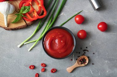 Bir kase lezzetli domates sosu ve gri arka planda farklı malzemeler.