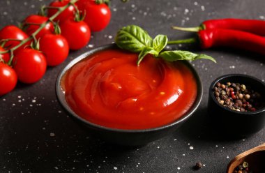 Bir kase lezzetli domates sosu ve siyah arka planda farklı baharatlar, yakın plan.