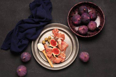Lezzetli prosciutto dilimleri, taze incir, zeytin ve krem peynirli siyah arka plan.