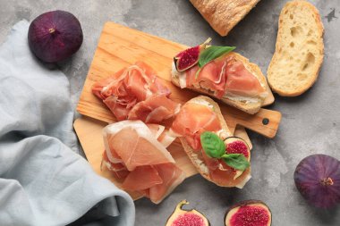 Lezzetli jambonlu ahşap ekmek dilimleri ve gri arka planda taze incir.