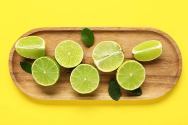 Tahta tepside taze limon dilimleri ve sarı arka planda yapraklar var.