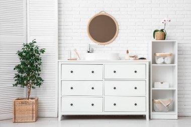 Lavabosu, aynası ve diş fırçası olan çekmeceler banyoda beyaz tuğla duvarın yanında.