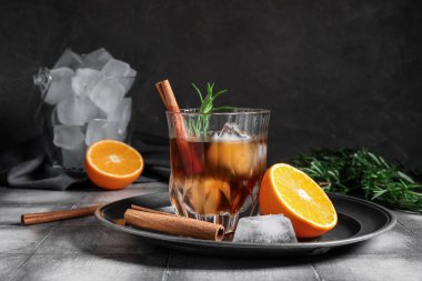 Bir bardak lezzetli eski moda biberiyeli kokteyl, portakallı ve tarçınlı çubuklar gri duvara karşı.