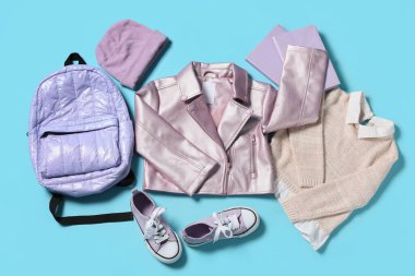 Sırt çantalı, şapkalı, spor ayakkabılı, süveterli ve mavi arka planda not defterli çocuk ceketi.