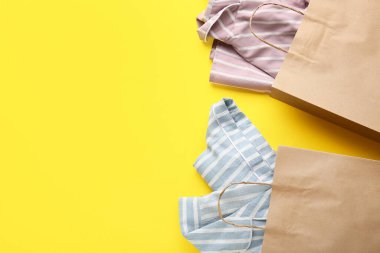 Sarı arka planda şık bluzlar olan kağıt alışveriş torbaları.