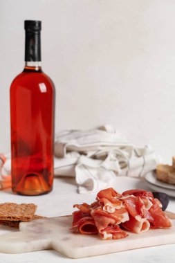 Lezzetli jambon dilimleri, çıtır ekmek ve beyaz arka planda bir şişe şarapla kesme tahtası.