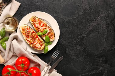 Domatesli patlıcan, fesleğen yaprağı ve siyah grunge arka planda bir sürahi yağ.