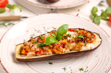 Beyaz ahşap arka planda içi doldurulmuş patlıcan, dereotu ve fesleğen yapraklı tabak.