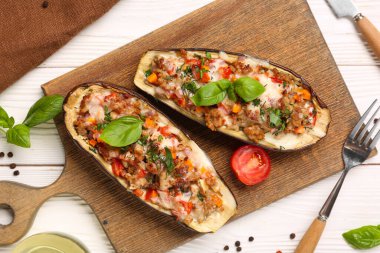 Beyaz ahşap arka planda içi doldurulmuş patlıcan, biber ve fesleğen yapraklarıyla dolu bir tahta.