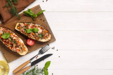 Beyaz ahşap arka planda içi doldurulmuş patlıcan, biber ve fesleğen yapraklarıyla dolu bir tahta.