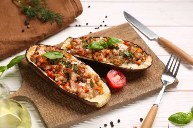 Beyaz ahşap arka planda içi doldurulmuş patlıcan, biber ve fesleğen yapraklarıyla dolu bir tahta.