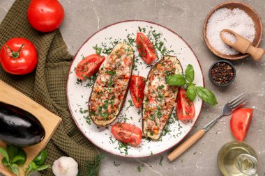 Doldurulmuş patlıcan, domates, dereotu, fesleğen yaprağı ve gri arka planda bir sürahi yağ.