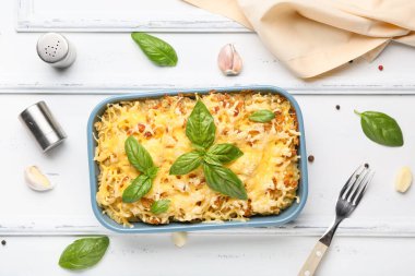 Beyaz ahşap arka planda fesleğen yapraklı ve peynirli makarna pişirmek.