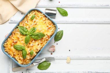 Beyaz ahşap arka planda fesleğen yapraklı ve peynirli makarna pişirmek.