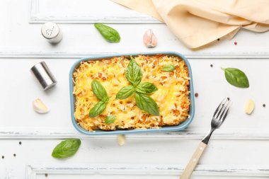 Beyaz ahşap arka planda fesleğen yapraklı ve peynirli makarna pişirmek.