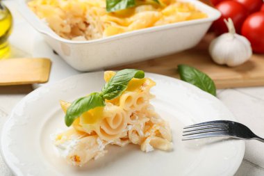 Beyaz fayans zemininde fırında makarna ve fesleğen yapraklarıyla dolu bir tabak.