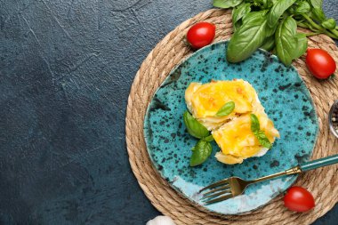 Mavi grunge arka planda fırında makarna, domates ve fesleğen yapraklarıyla dolu bir tabak.