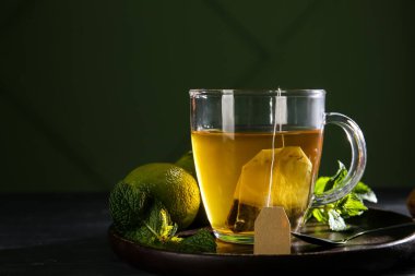 Koyu arka planda, ahşap masada limon ve nane yapraklı bir fincan sıcak çay.