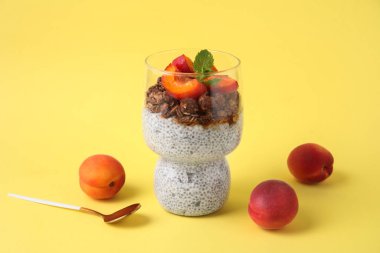 Bir bardak lezzetli chia tohumu pudingi granola ve sarı arka planda kayısı.