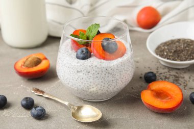 Bir bardak lezzetli chia tohumu pudingi yaban mersinli ve kayısılı gri arka planda.