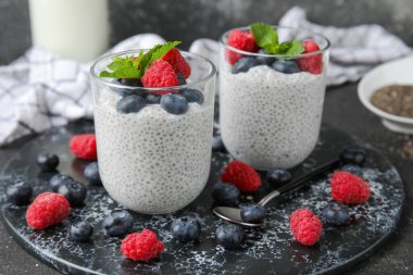Bardaklar dolusu lezzetli chia tohumu pudingi yaban mersini, ahududu ve siyah grunge arka planda nane yaprağı.