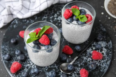 Bardaklar dolusu lezzetli chia tohumu pudingi yaban mersini, ahududu ve siyah grunge arka planda nane yaprağı.