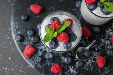 Bardaklar dolusu lezzetli chia tohumu pudingi yaban mersini, ahududu ve siyah grunge arka planda nane yaprağı.