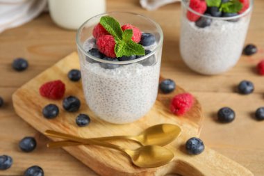 Bardaklar dolusu lezzetli chia tohumu pudingi yabanmersini, ahududu ve ahşap zemin üzerinde nane yaprağı.