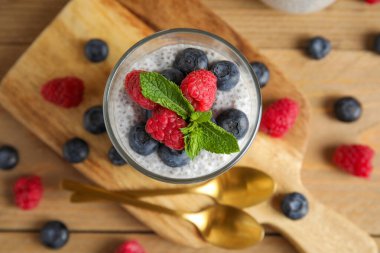 Bir bardak lezzetli chia tohumu pudingi yaban mersini, ahududu ve ahşap zemin üzerinde nane yaprağı.