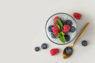 Beyaz arka planda yaban mersini, ahududu ve nane yapraklı lezzetli chia tohumu pudingi.