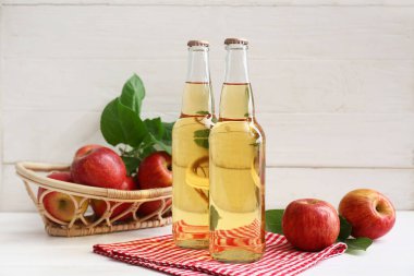 Beyaz ahşap arka planda elma şarabı şişeleriyle taze meyveler.