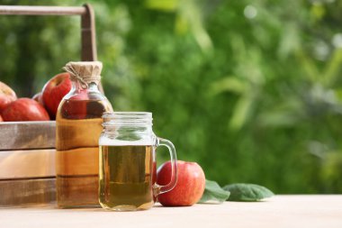 Şişeli taze meyveler ve açık bej masa üzerinde elma şarabı kavanozu.