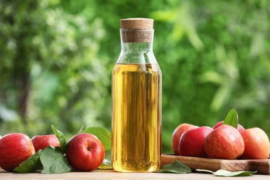 Dışarıdaki bej masada elma şırası şişesiyle taze meyveler.