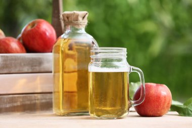 Şişeli taze meyveler ve açık bej masa üzerinde elma şarabı kavanozu.