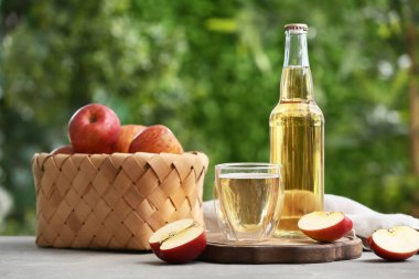 Şişeli taze meyveler ve açık havada gri masada bir bardak elma şarabı.