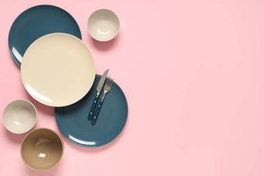 Pembe arka planda gümüş çatal bıçaklı farklı temiz tabaklar.