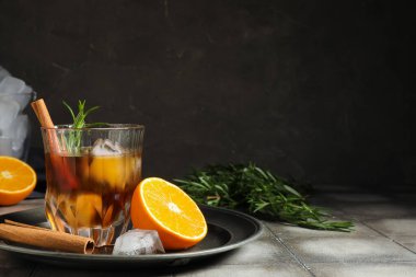 Bir bardak lezzetli eski moda biberiyeli kokteyl, portakallı ve tarçınlı çubuklar gri duvara karşı.