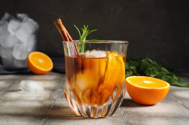 Bir bardak lezzetli eski moda biberiyeli kokteyl, portakallı ve tarçınlı çubuk gri duvara karşı.
