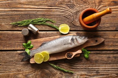 Tahta kesme tahtasında taze deniz kabuğu balığı ve ahşap arka planda farklı baharatlar var.