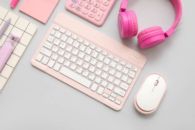 Gri arkaplanda modern bilgisayar klavyesi, fare, kulaklık ve kırtasiyesi olan bilgisayar