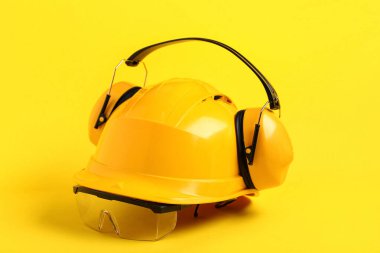 Sarı arka planda işitme koruyucuları ve güvenlik gözlükleri olan sert şapka