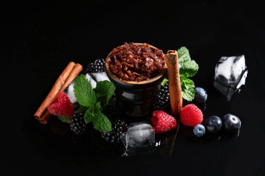 Böğürtlen, buz küpü, tarçın çubuğu ve siyah arka planda nane yapraklı nargile kase tütün.