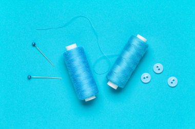 Mavi zemin üzerinde top iğneleri ve düğmeleri olan iplik makaraları