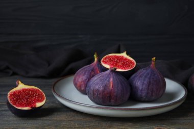 Siyah ahşap masada taze incir tabağı, yakın plan.